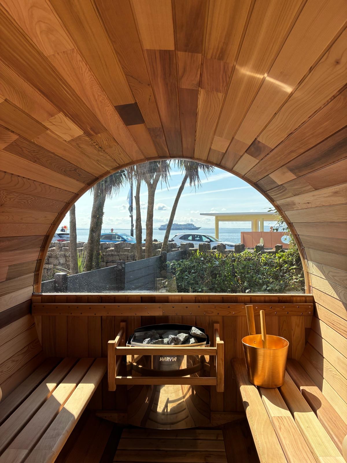 Interior of the Blue Wellness outdoor barrel sauna at Galway Bay Hotel, featuring wood seating, sauna heater and sea views.